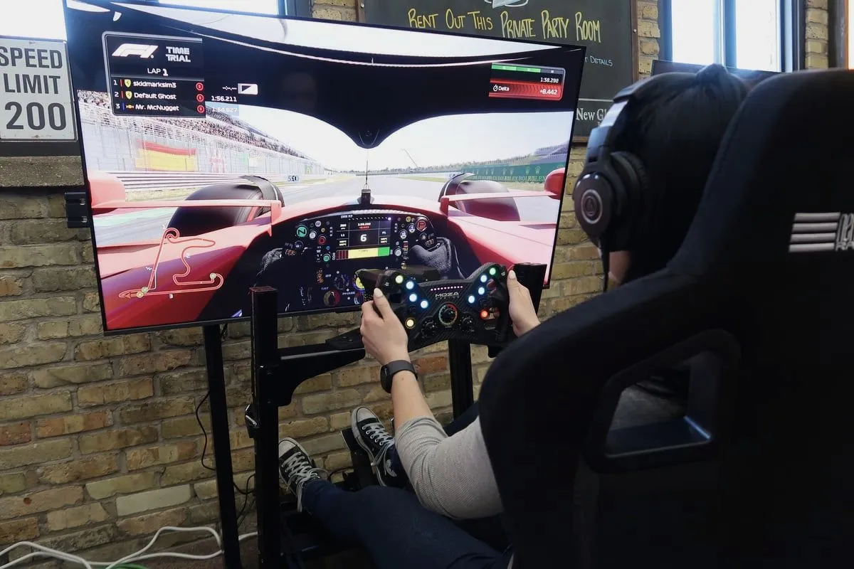 A guest drives a Skid Mark racing simulator while the lap runs on a large screen